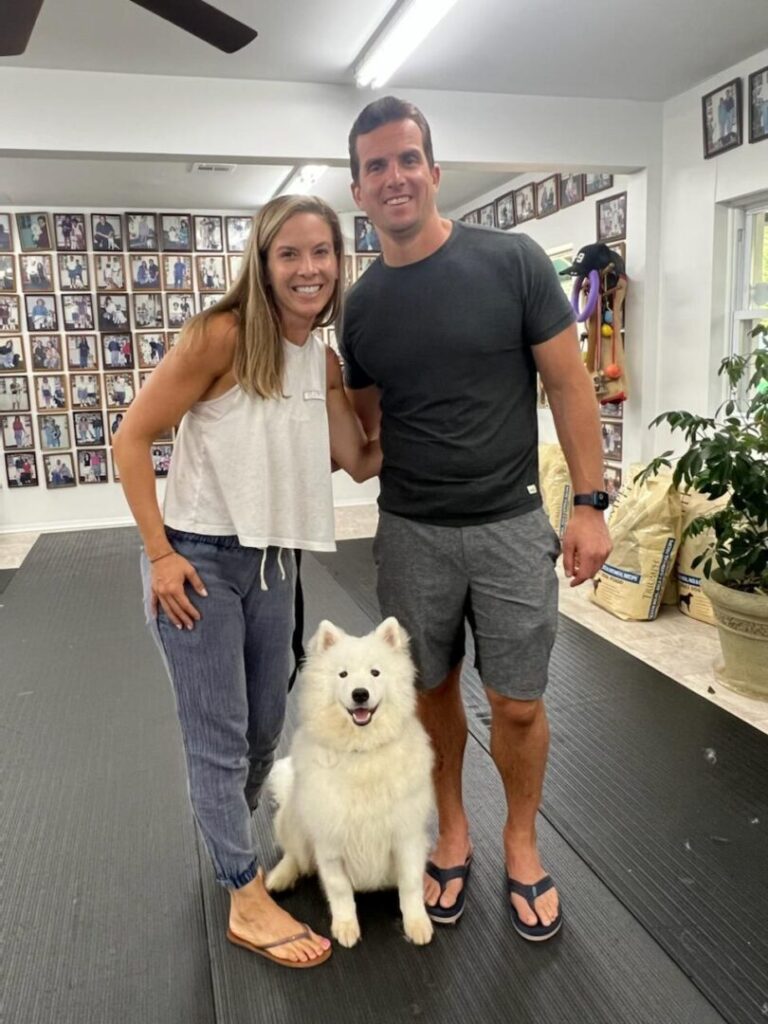 a man and woman standing next to a white dog