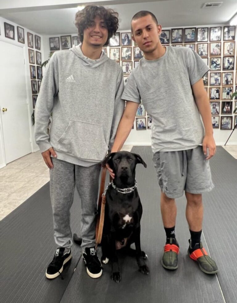 two young men standing next to a black dog