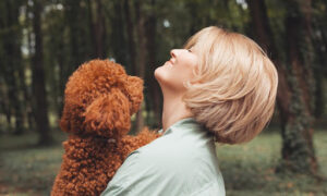 a woman holding a brown poodle in a forest