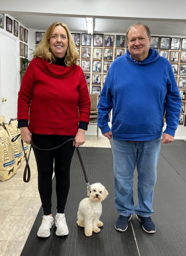 a man and woman walking a small white dog on a leash