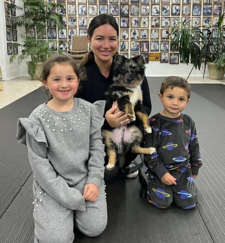 a woman kneeling down next to two children and a dog
