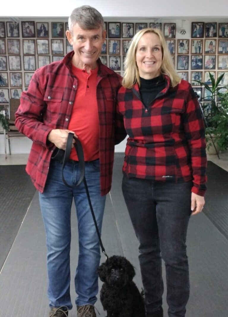 a man and woman standing next to a black dog