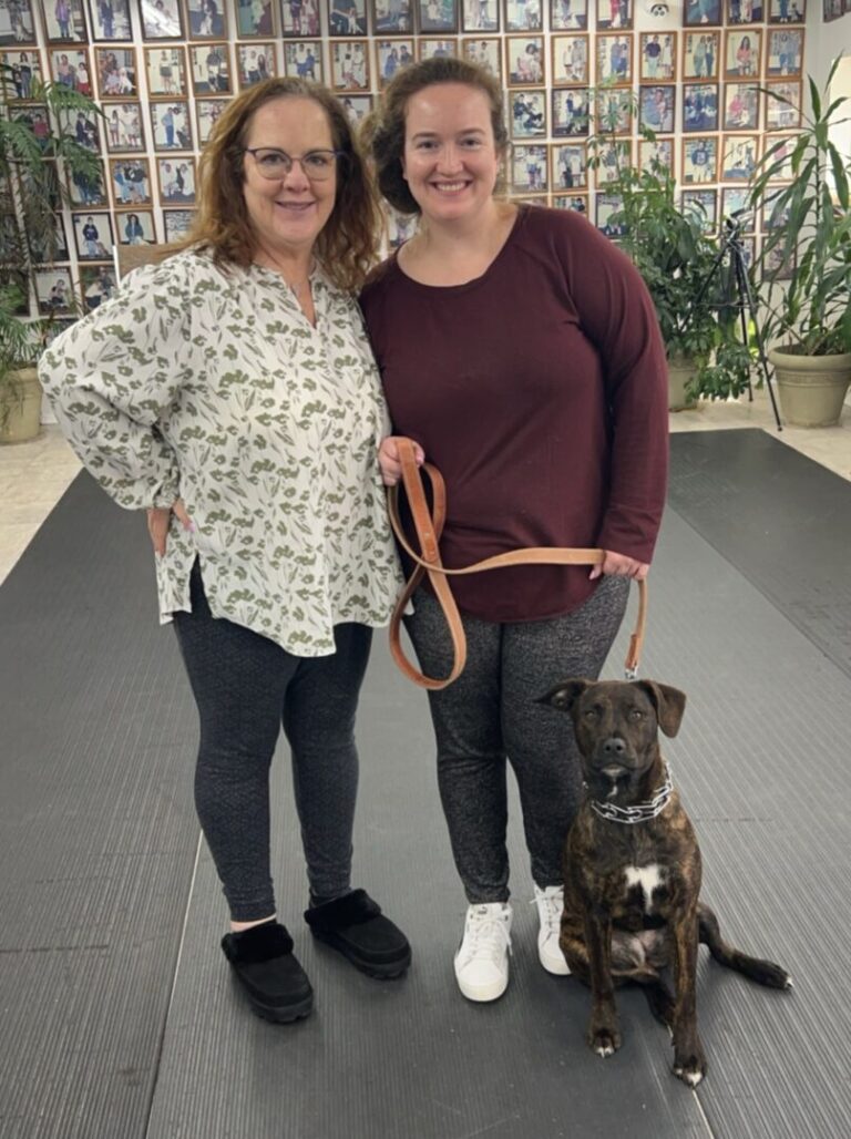 two women standing next to a dog on a leash