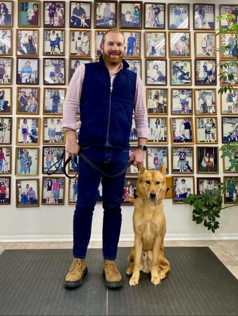 a man standing next to a dog in front of a wall of pictures