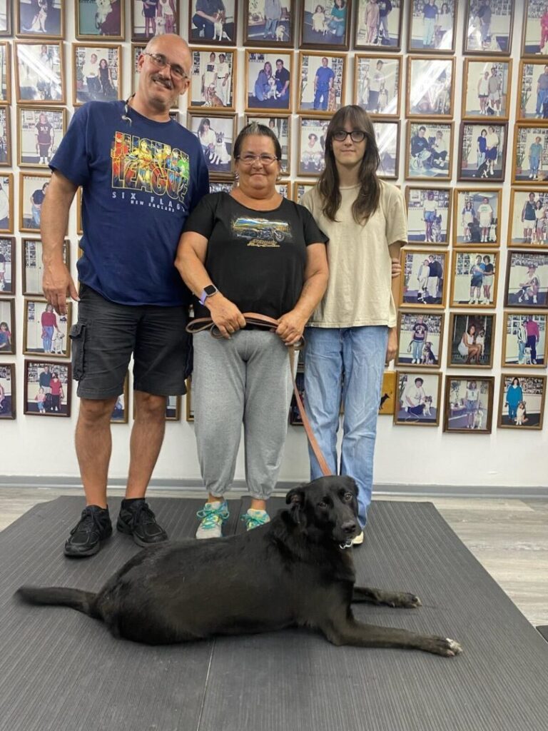 a man and a woman standing next to a black dog