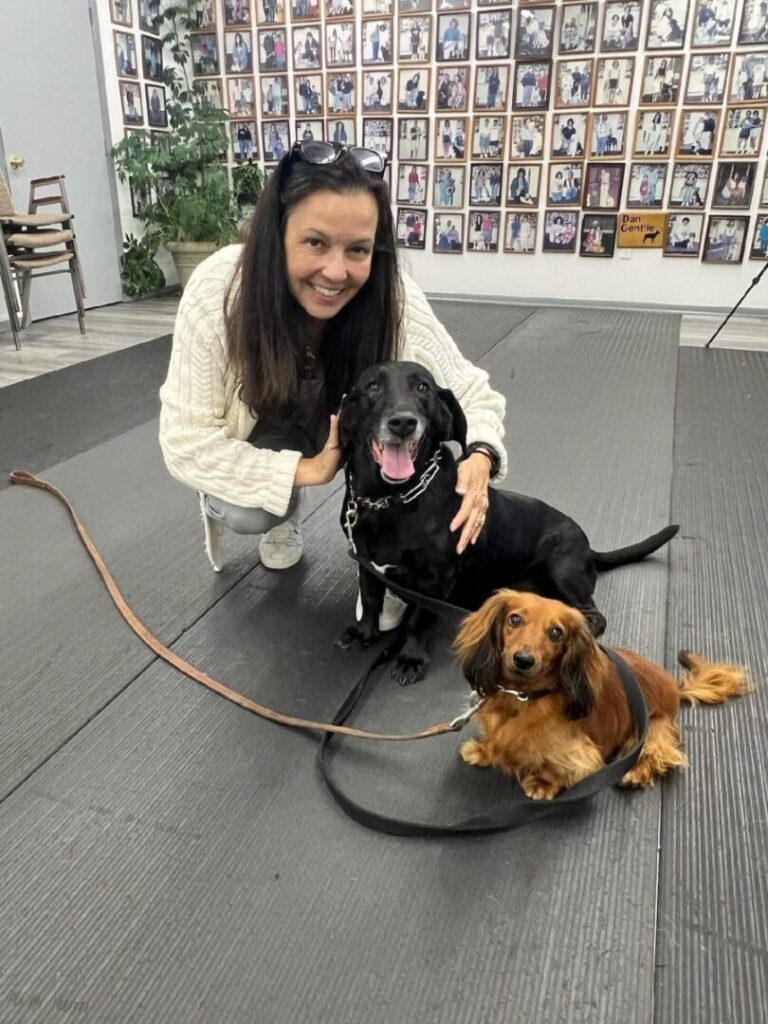 a woman kneeling down with two dogs on a leash